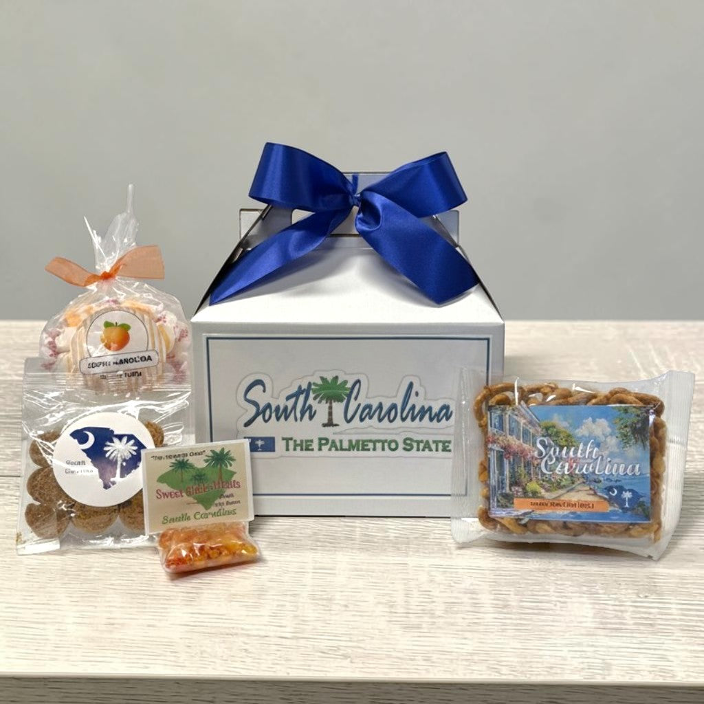 Gift box with South Carolina-themed products including a peach candy, cookies, and a bag of candy on a light surface.